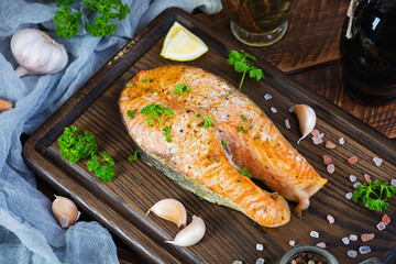 Baked salmon steak with herbs on wooden cutting board. Grilled salmon with salt and pepper