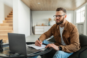Fototapeta na wymiar Man Using Laptop And Taking Notes Working Online At Home