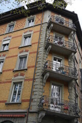 Old brick residential building with windows and balconies. Cutout of a facade with a low angle view. There are chairs and tables on the balconies.