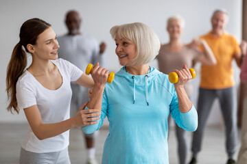 Female fitness coach helping senior woman while exercising