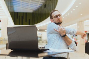 Freelancer man stretching arms while working at laptop