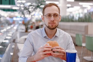 Office worker eating fast food burger and drink soda at food court in mall at lunch