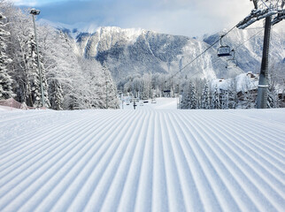 Snowy groomed slope with velvet lines in ski resort at mountains and chairlift background