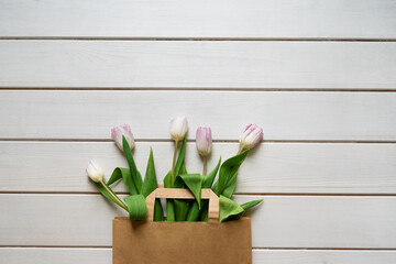 Spring bouquet of pink tulips in beige paper bag on white wooden background