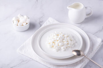 Fresh cottage cheese grain in a white bowl and marshmallows. Curd in granules with cream. Copy space