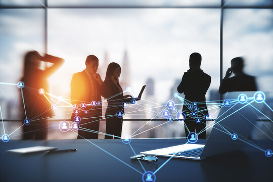 Businesspeople working together in modern office with laptop on desktop and abstract glowing polygonal network with people icons and blurry city view. 