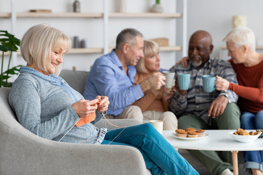 Relaxed senior lady knitting, sitting by her multiracial friends