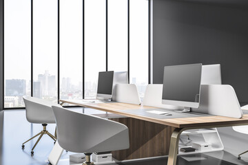 Fototapeta premium Contemporary coworking office interior with wooden furniture, equipment, computer monitors and window with blurry city view and daylight. 3D Rendering.