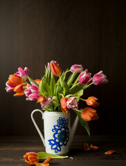 pink and orange colored tulips in vase in front of a dark brown wooden wall