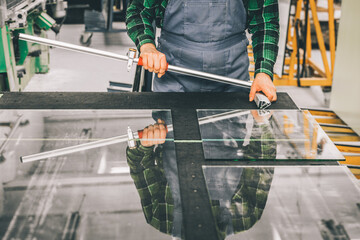 Glazier standing over a cut glass pane with specialized cutting equipment, Cutting glass panels in...