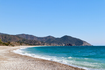 Fototapeta premium pebble beach of Cirali, Turkey and mediterranean sea with mountain and clouds in spring sunny day