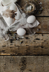 Easter rustic flat lay, space for text. Natural eggs in tray, feathers, willow branches, nest on aged wooden table. Stylish Easter rural still life. Simple aesthetics. Happy Easter