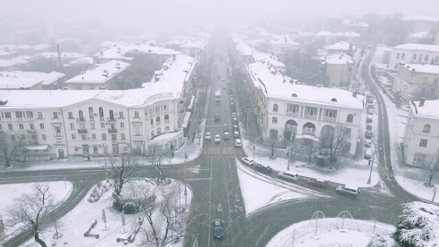 Cinematic flight over the snow-covered streets of the city. Roads and trees are covered with snow. Strong blizzard. Winter fairy tale in the city from the air.