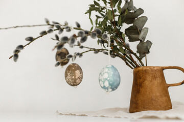 Easter rustic still life. Natural dyed easter eggs, willow branches in vase, feathers, nest on linen napkin on aged wooden table. Happy Easter! Simple stylish easter decoration on table aesthetics