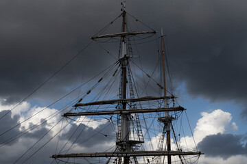 Top of ship mast against a clearing sky. Dramatic dark clouds frame the mast's tip  and a window of blue sky in the centre. Fluffy white and grey clouds beneath blue sky.