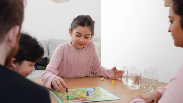 Mixed-race family spending time at home. Mother, father and kinds sitting together at the table and playing with board game. Real life, diversity, digital detox and unplugging from technology. 4K UHD