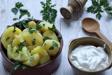 Cooked potatoes in brown clay bow decorated with parsley, sauer cream and wooden spoon next to on the table 