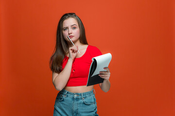 Pensive young girl make notes in notepad, create ideas for project, make schedule, to do list on orange background