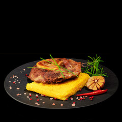 Fried polenta with rosemary, garlic, and spices. A steak lies on top. On a black plate