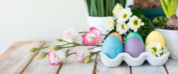 Easter composition, holiday home decor. Colourful eggs, flowers on the white wooden table. Copy space for text banner