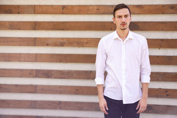 emotions, gesture, lifestyle and people concept - Disappointed slumped Caucasian guy in a white shirt standing outdoors looking at the camera on a brown ribbed background with copy space