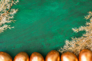 Golden Easter eggs and golden branches, reeds on a green watercolor background. Banner. Layflat. Space for text 