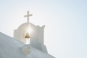 White Orthodox Church belfry with cross and bell in sunshine on sky background. Santorini island, Greece