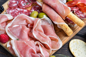 Italian food antipasti prosciutto ham, salami, olives and grissini bread sticks. cheese on a board...