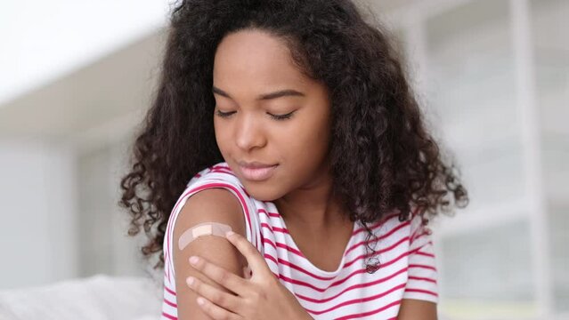 vaccinated African American woman showing arm with medical plaster patch Plaster On Shoulder, black female after getting vaccine dose against covid. Healthcare immunization, coronavirus vaccination