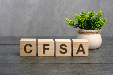 cfsa word is written on wooden cubes on a gray background. close-up of wooden elements. In the background is a green flower in a tub