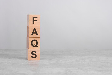 wooden cube on a concrete surface with text FAQS. copy space on right for design, gray background