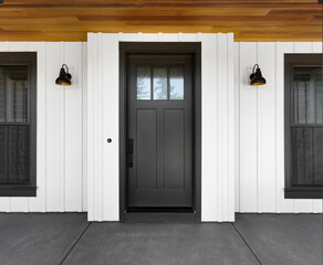 Front door to modern farmhouse home. Home exterior with white vertical wood siding and black front door.  Sconce lights flank door on both sides.