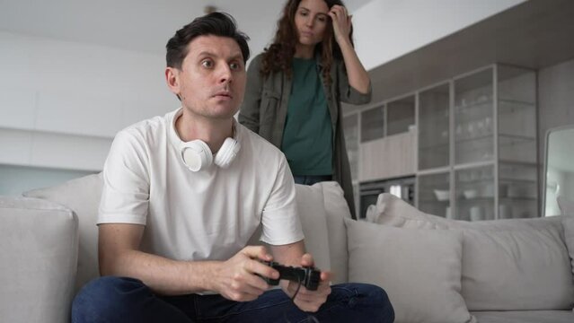 Wife scolds her husband for playing video games and not paying attention to her while sitting on the couch in the living room