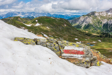 Red and white marking of the hiking trail in the Austrian Alps. Sunny mountain panorama with snow in the foreground. - 485427495