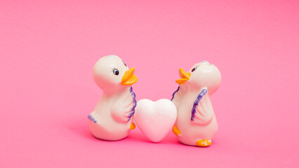 two ceramic ducks and white heart on pink background. Symbols of love and fidelity. Cute greeting card for wedding invitation, for Valentine's day. Illustration of the feeling of love between two.