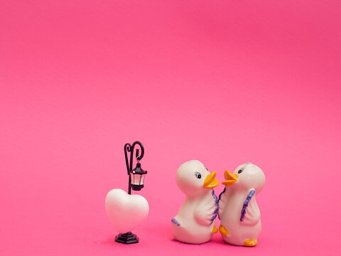 Two cute ducks toys look at each other with street lamp and heart on pink background. Illustration of the feeling of love between two people.