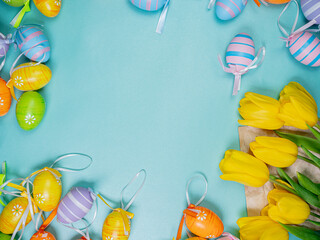 Several spring yellow tulips lie on a blue background next to Easter eggs