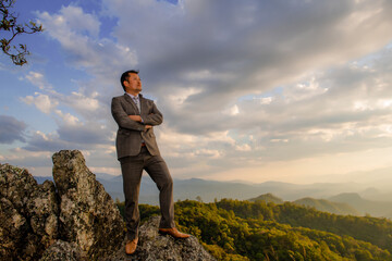 Obraz premium Successful business man standing on a peak of the mountain and purposefully looking away.