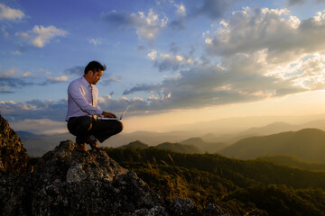 Man working outdoors with laptop sitting in mountains. Concept of remote work or freelancer lifestyle.Hiker tourist enjoying valley view sunset.