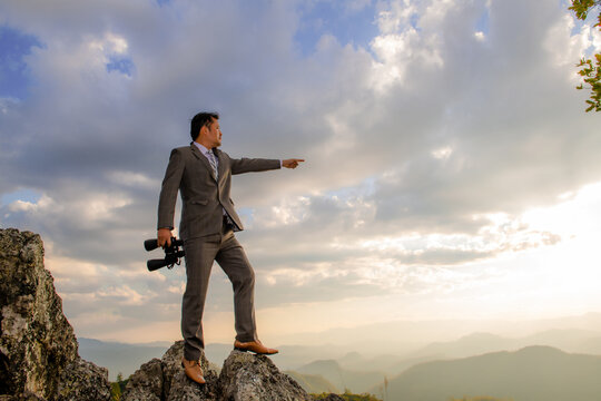 Young businessman using binoculars from a rock over a mountain