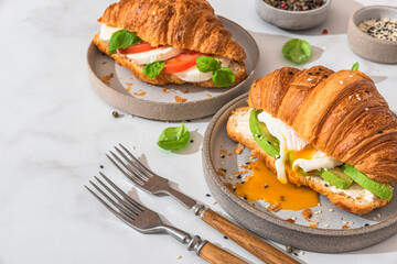 Tasty breakfast with croissant sandwiches with poached egg, avocado, soft cheese, mozzarella and tomato in a plate