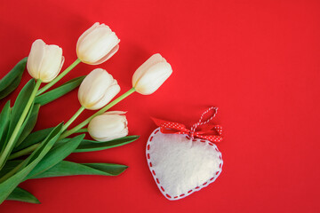 Fototapeta na wymiar White tulips and toy heart on red background. Valentines day concept. Top view, flat lay