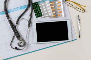 Doctor planning appointment on calendar with health stethoscope, digital device table and pills