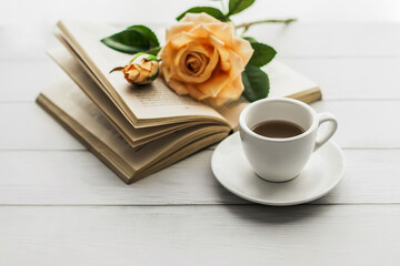 Morning coffee. A cup of coffee on a white wooden table and an open book with a rose flower. Lifestyle, romantic mood. Cozy morning