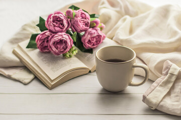 Morning coffee. A cup of coffee on a wooden table and an open book against a background of a bouquet of spring flowers. Still life concept. Cozy morning.