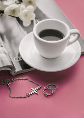 The atmosphere of a romantic morning, morning coffee. Spring flowering branch on a magazine, a cup of coffee and women's jewelry scattered on the table.Lifestyle. Selective focus.