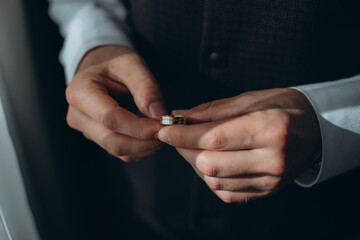 The groom holds the gold wedding rings with his fingers.