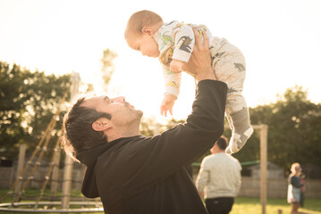 A father holds his baby up in the air in a public play park in a sunny day in Edinburgh, Scotland, United Kingdom