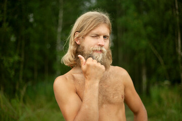 White man naked from waist up. Guy in nature in woods. Blonde with thick beard and long hair.