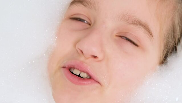 Portrait of cheerful teen girl lying in bath with thick soap foam and looking in camera. Concept of child hygiene and health care at home. Child having fun and playing at home.